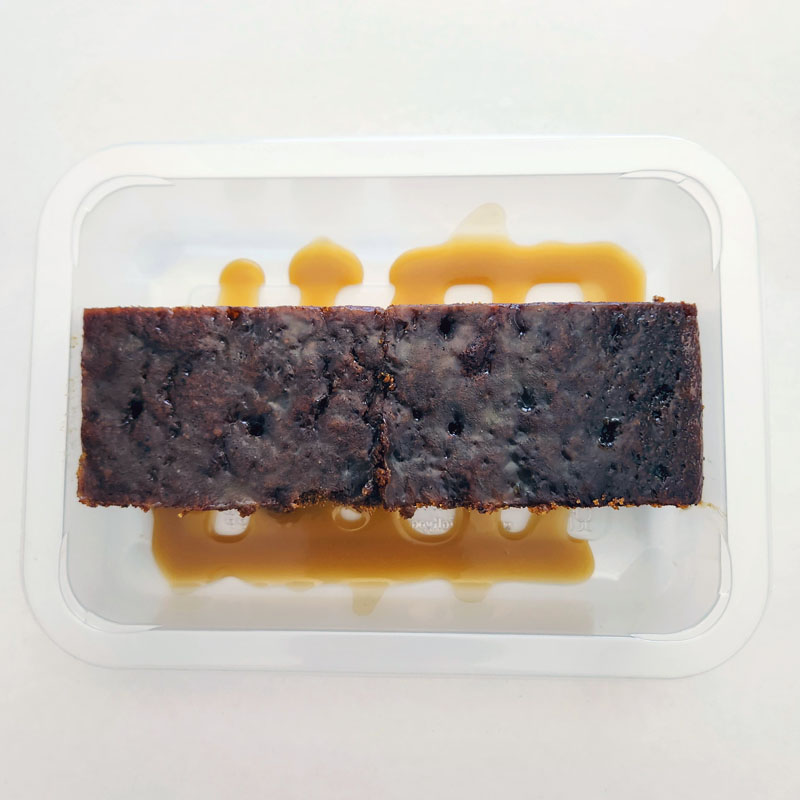 In a tray, rich sticky date pudding, served warm with a silky butterscotch sauce that cascades over each slice, creating the perfect comforting classic dessert.